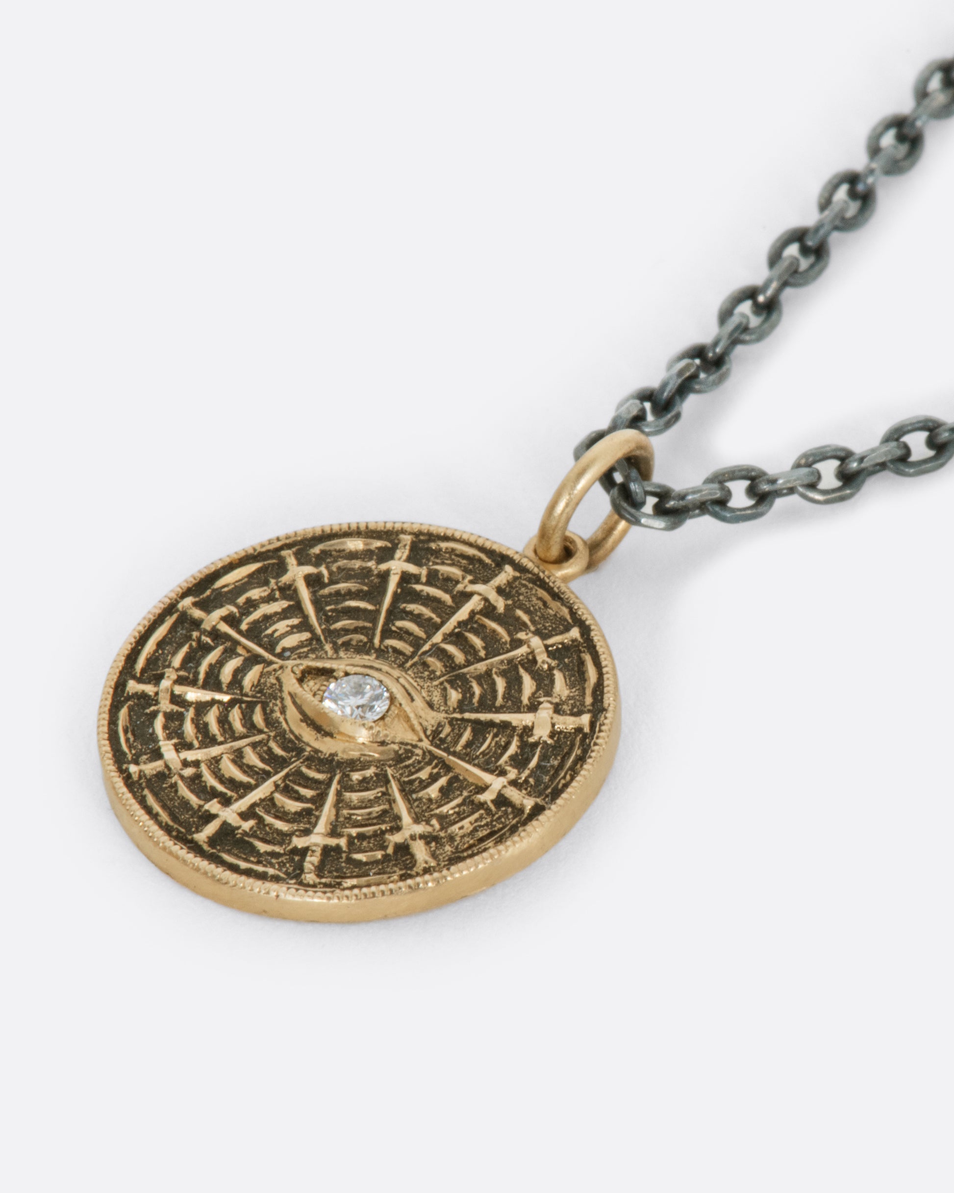 An oxidized sterling silver necklace with a yellow disc pendant, with a diamond eye at its center and swords radiating around it.