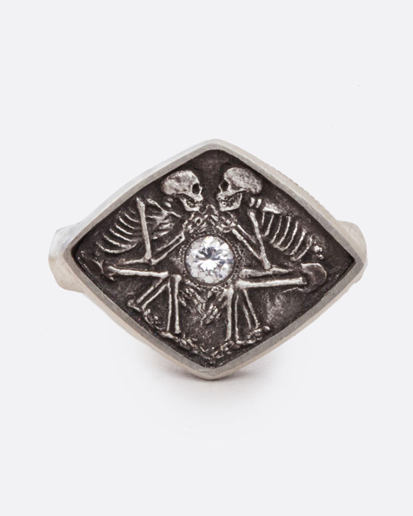 A sterling silver ring with two skeletons facing each other, lying in lovely death with a round diamond resting in their hands, glowing between them