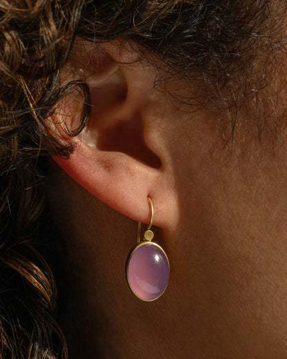 Lola Brooks earring in 18k yellow gold worn on an ear, an oval purple chalcedony cabochon in a gold bezel on a hook wire
