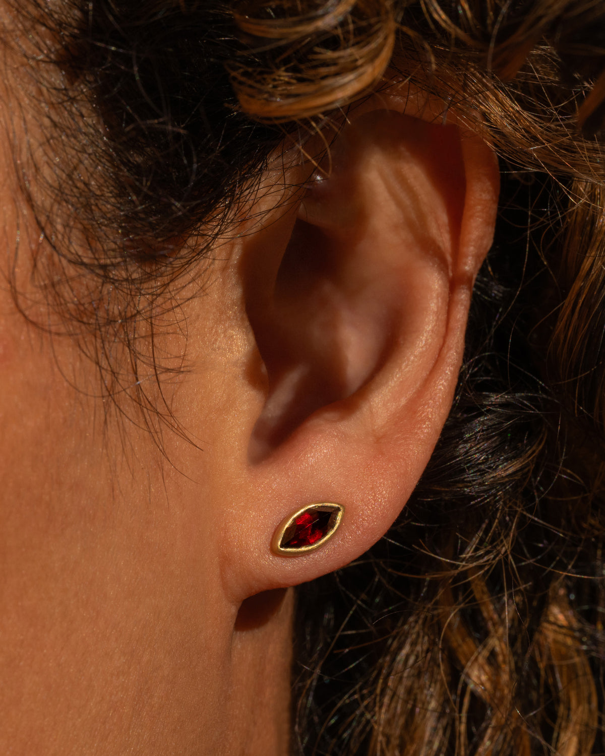 Lola Brooks stud earring in 18k yellow gold worn on an ear, an antique navette-shaped red garnet in a smooth gold bezel