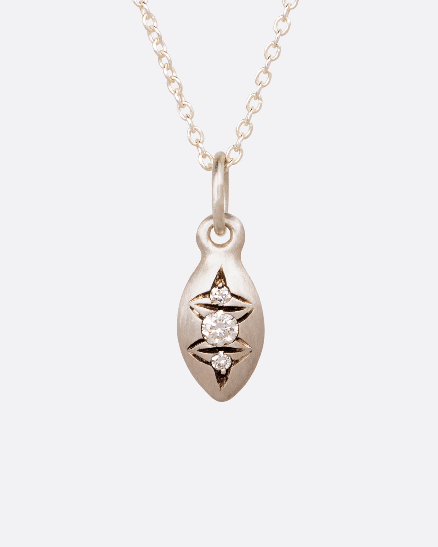 A pepita seed shaped pendant with three diamonds and oxidized etching.