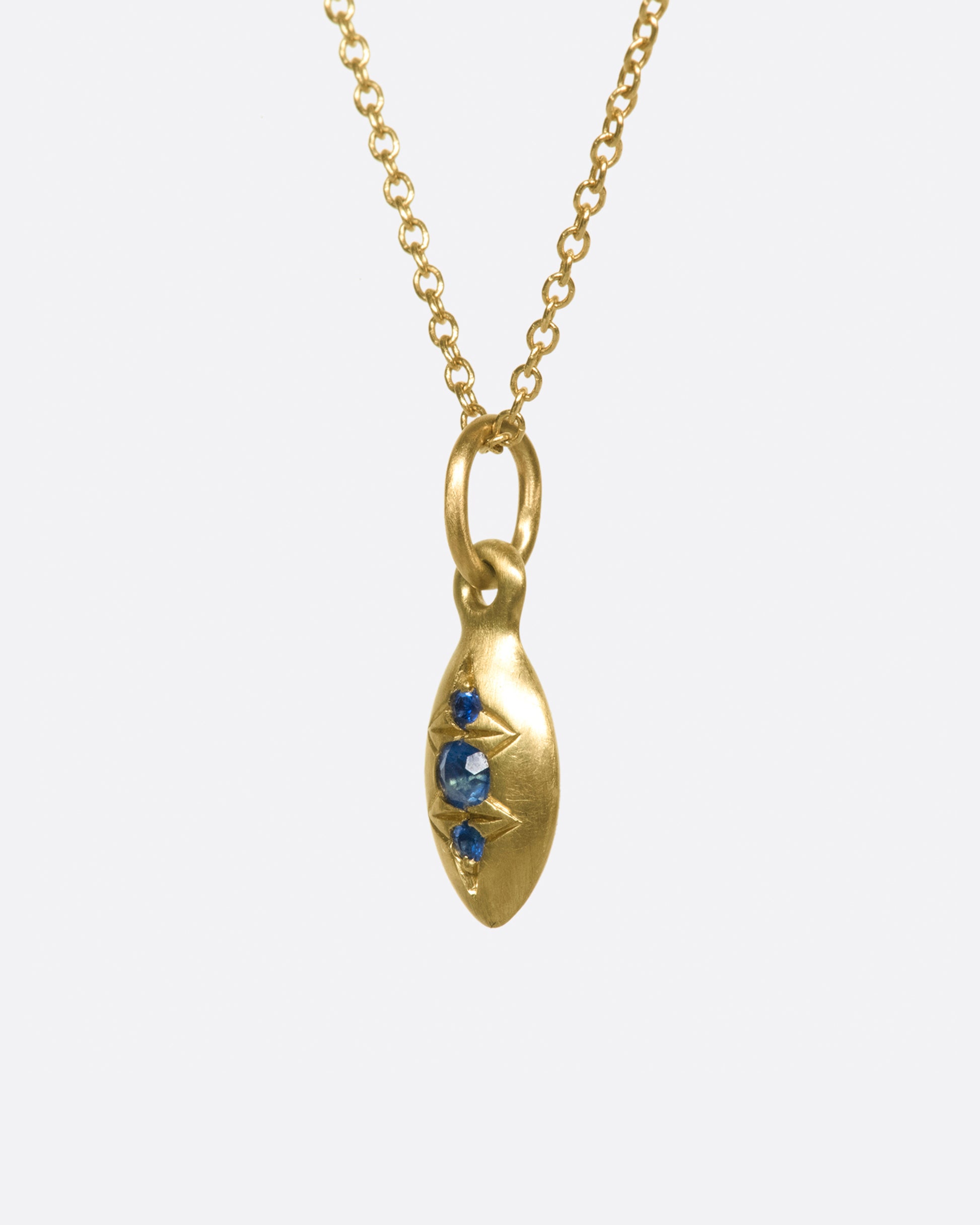 A seed-shaped, brushed gold pendant necklace with three vibrant blue sapphires.