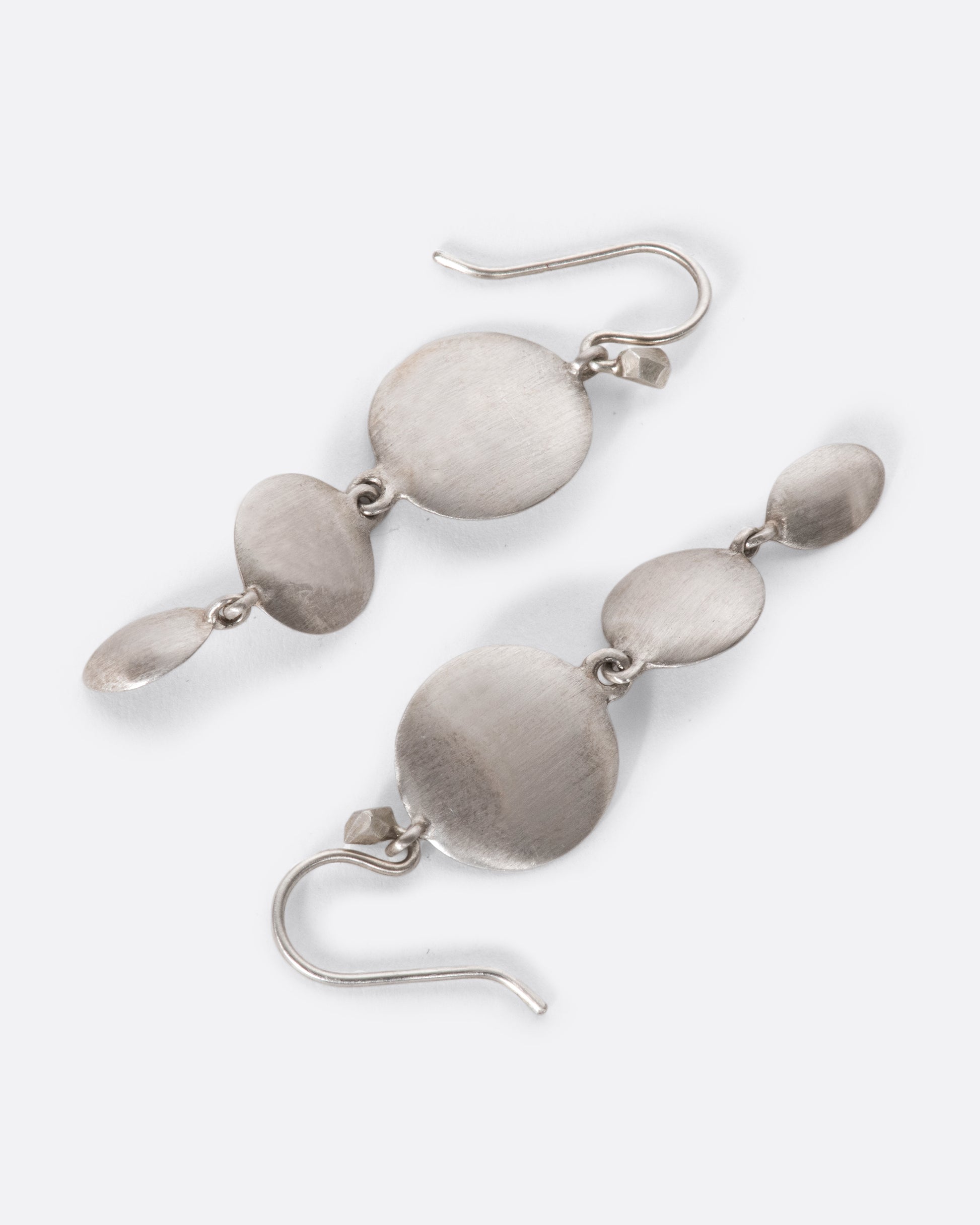 A pair of sterling silver triple drop dangles that juxtapose smooth, flat circular and oval faces against razor-thin edges