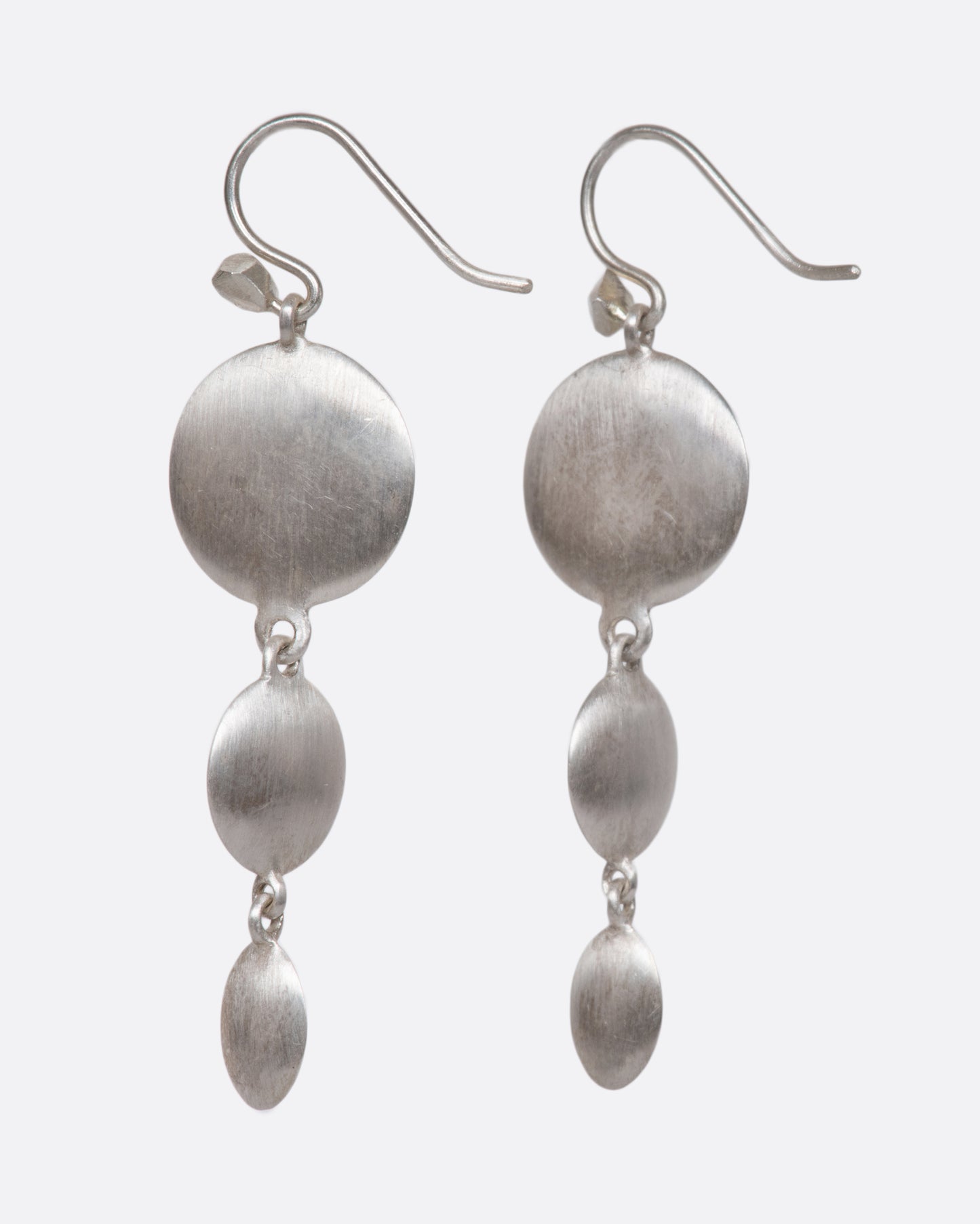 A pair of sterling silver triple drop dangles that juxtapose smooth, flat circular and oval faces against razor-thin edges