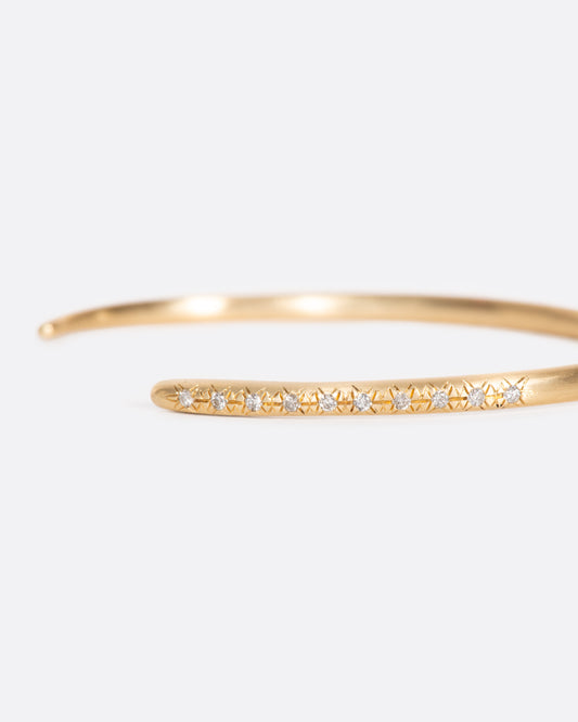 This brushed gold cuff bracelet tapers at one end and is dotted with ten light gray diamonds at the other.