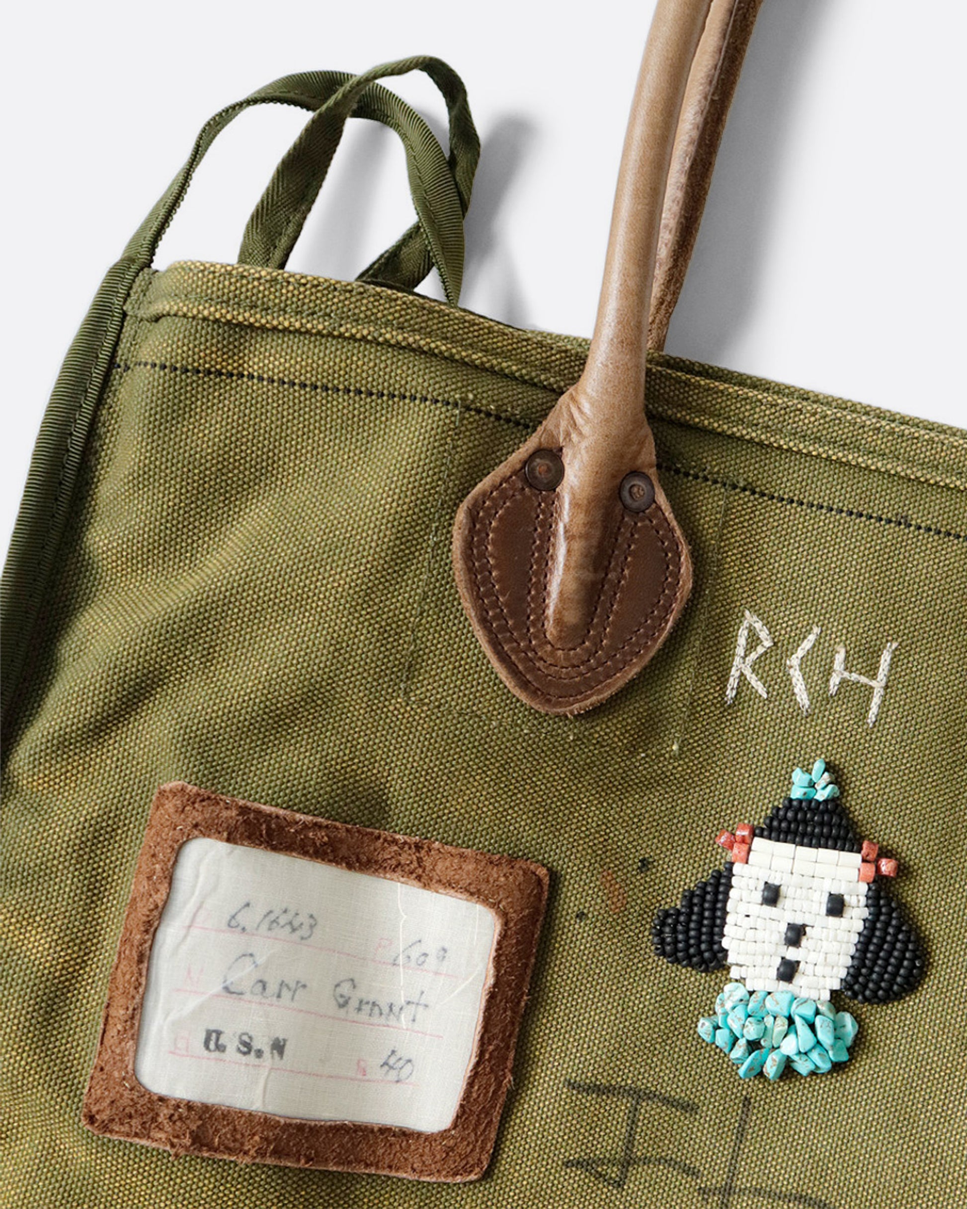 Canvas tote with patches and beaded embroidery. Close up of leather handle.