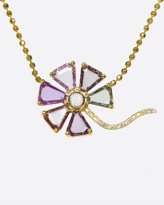 A close up view of a flower pendant with sapphire petals, diamond stem, and opal center on a gold ball chain.