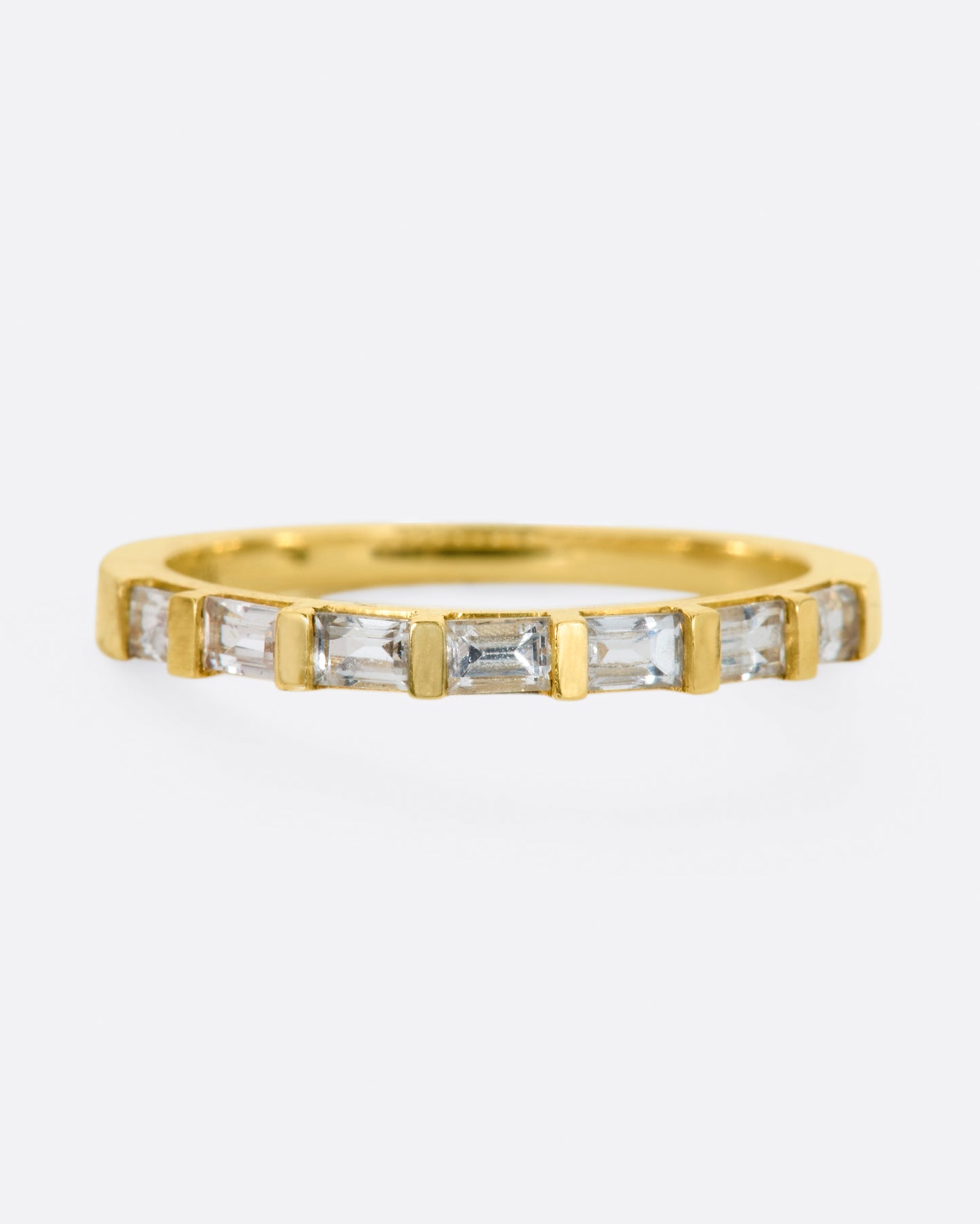 A yellow gold band with seven white sapphire baguettes covering half of the ring.