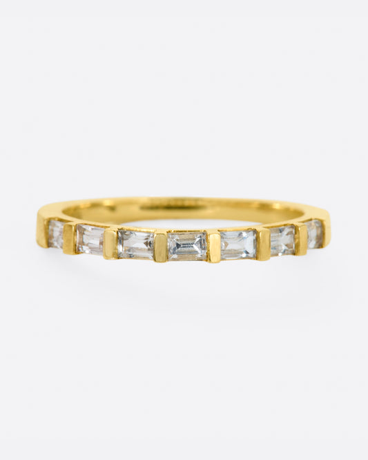 A yellow gold band with seven white sapphire baguettes covering half of the ring.