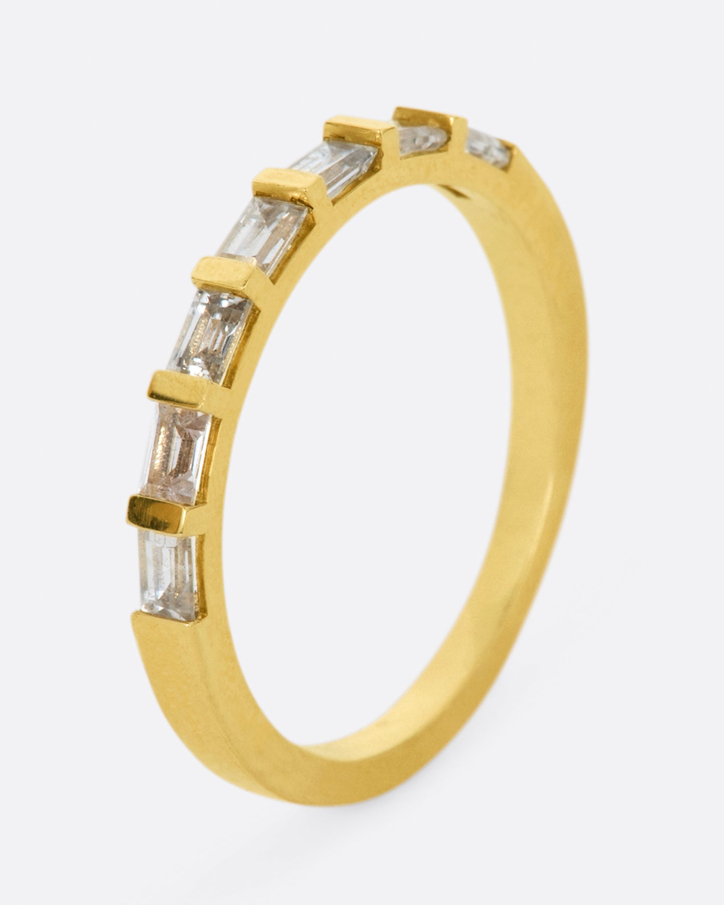 A yellow gold band with seven white sapphire baguettes covering half of the ring. Shown from the side.