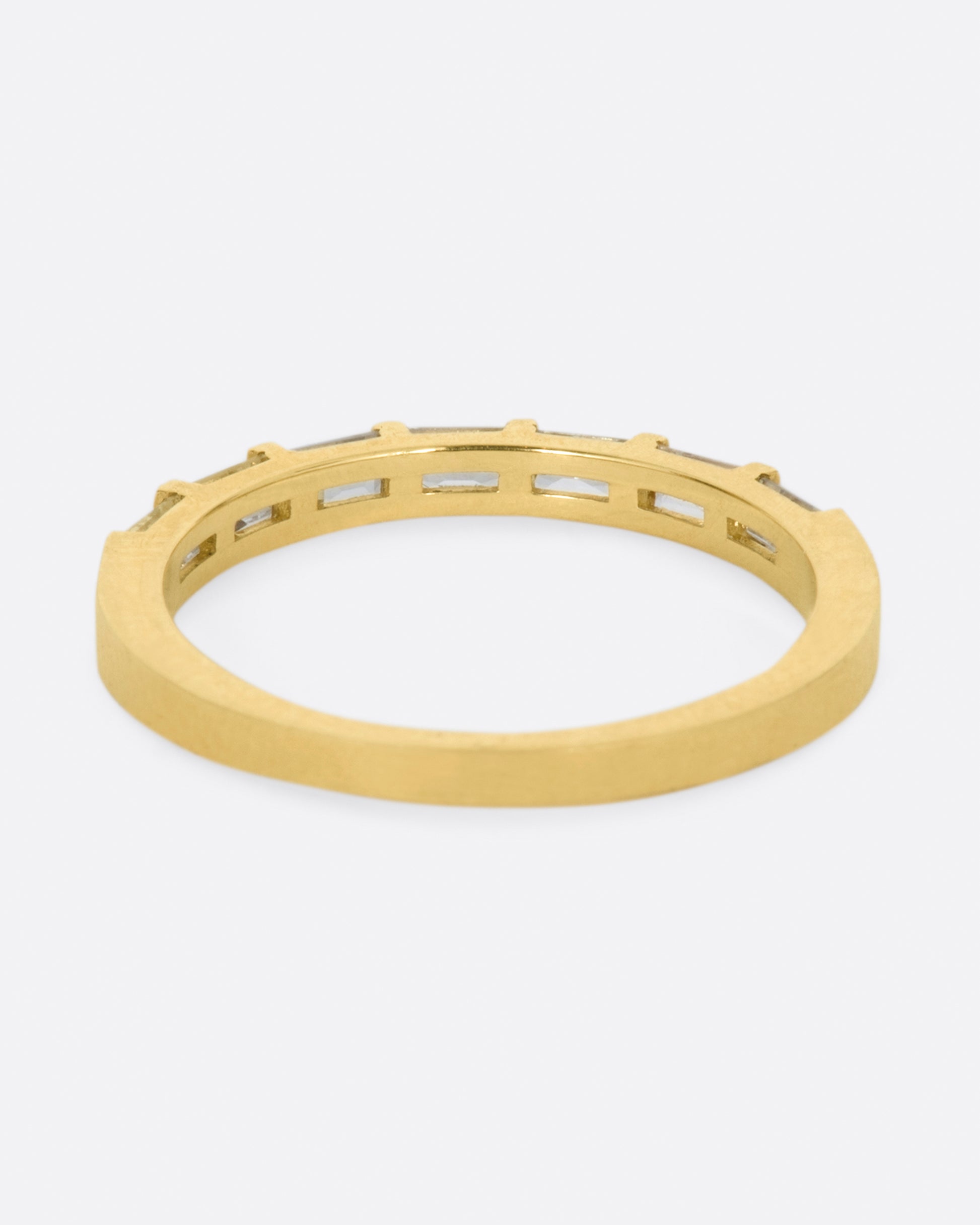 A yellow gold band with seven white sapphire baguettes covering half of the ring. Shown from the back.