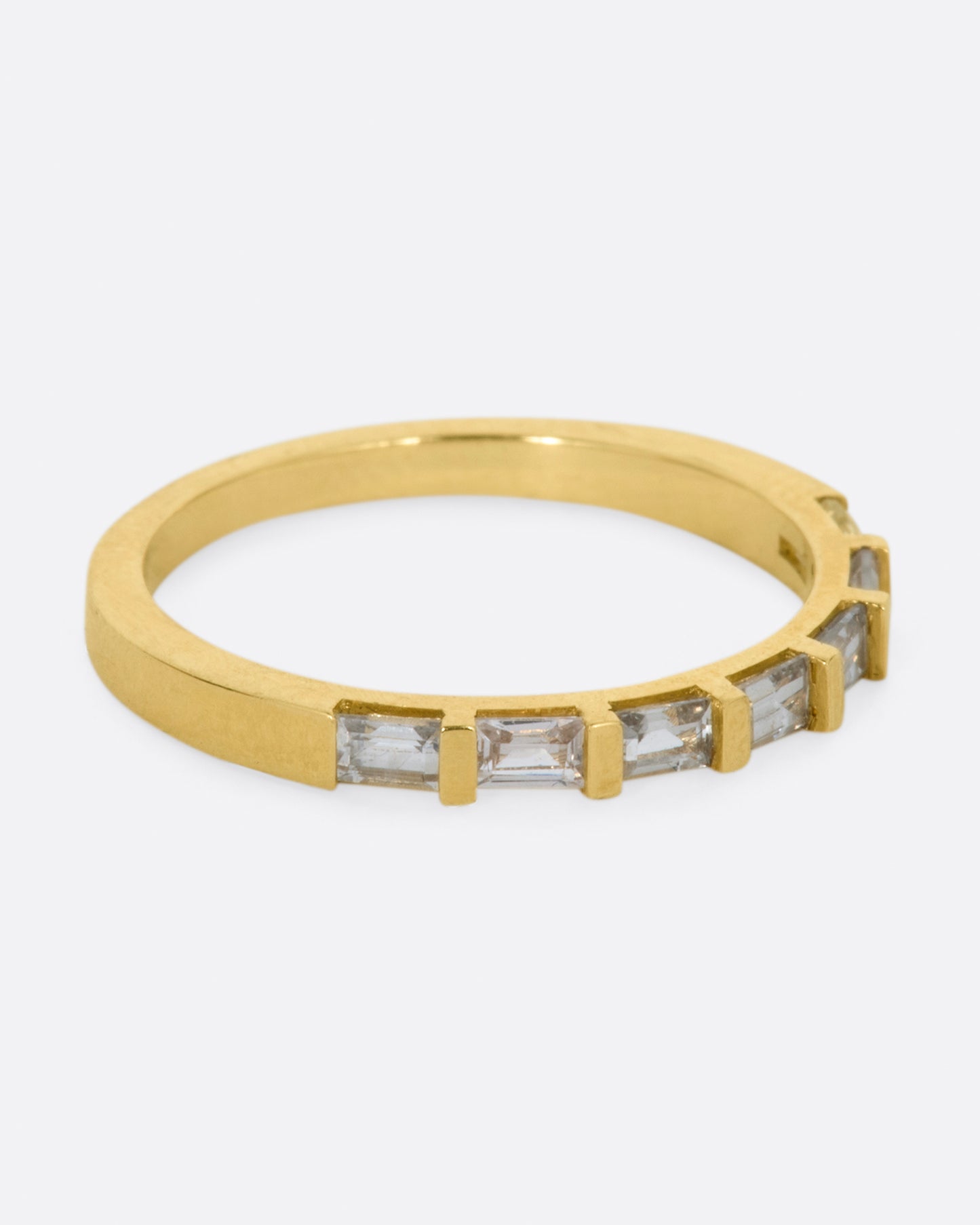 A yellow gold band with seven white sapphire baguettes covering half of the ring. Shown from the side.