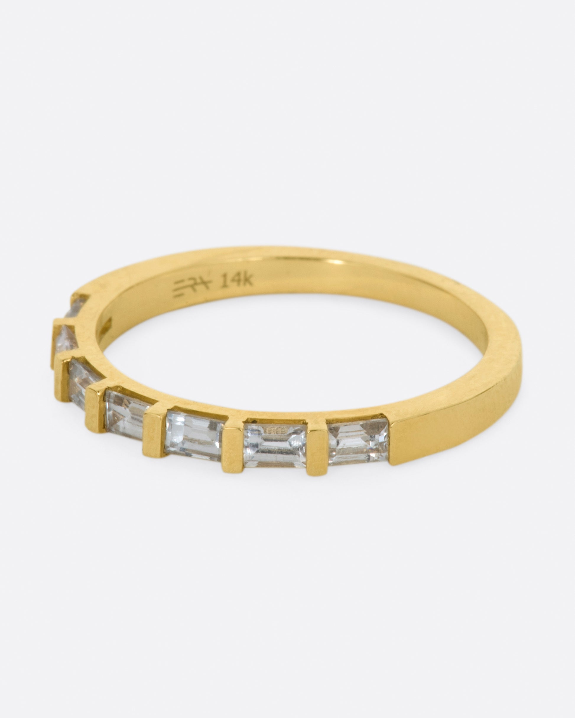 A yellow gold band with seven white sapphire baguettes covering half of the ring. Shown from the side.