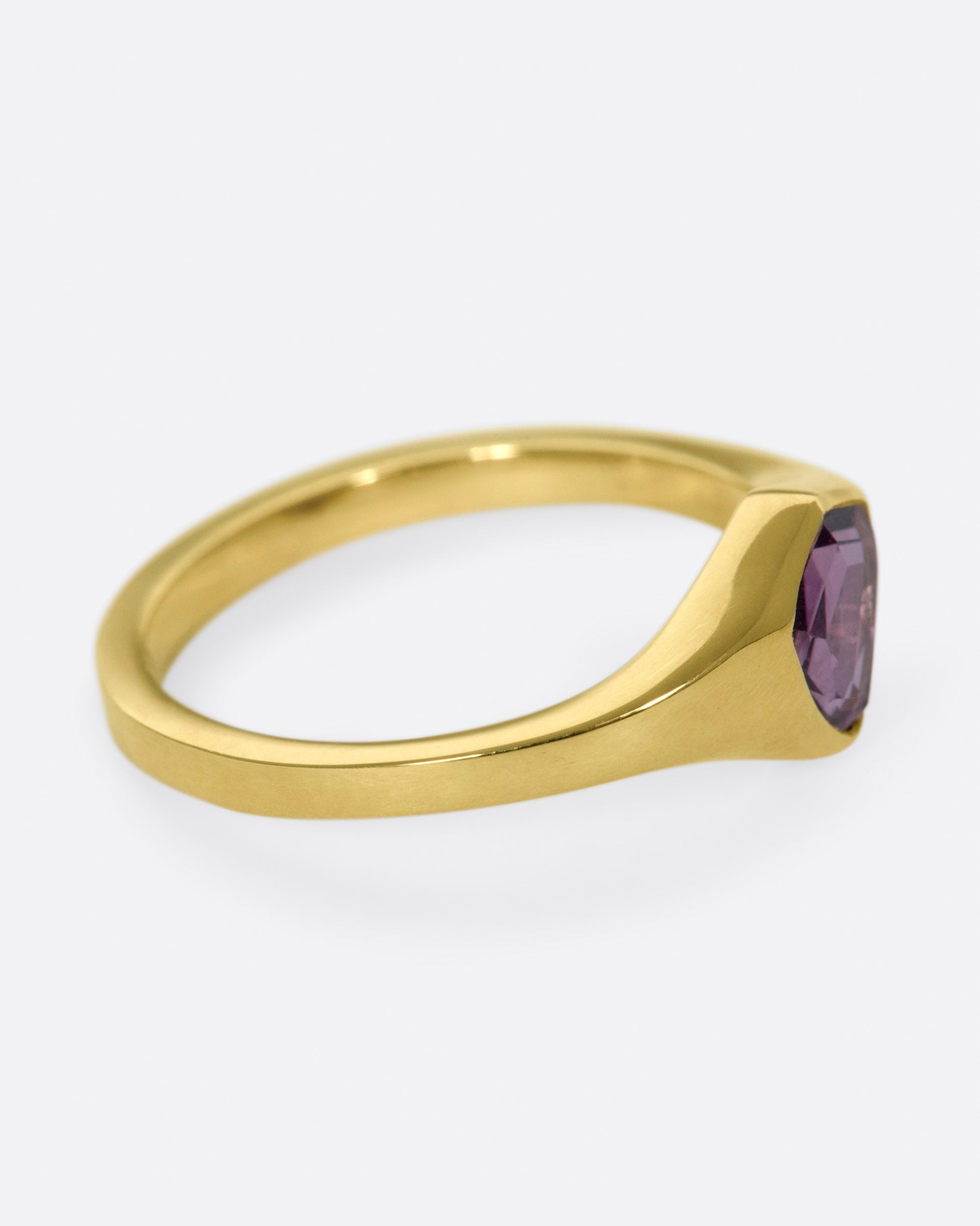 A classic, polished gold signet ring with a burgundy sapphire at its center.