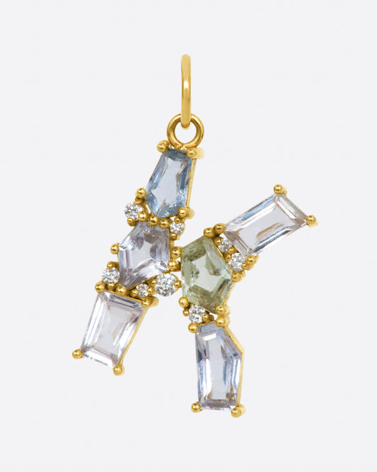 A yellow gold large letter K pendant lined with six pale pastel sapphires and dotted with diamonds.