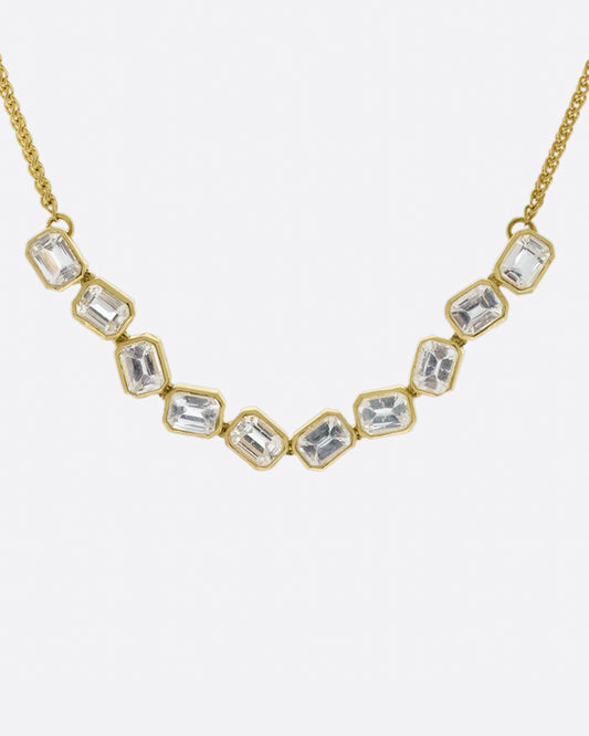 A chain necklace with a section of ten bezel set, emerald cut, white sapphires each connected to its neighbor by a hinge so the whole piece moves fluidly.