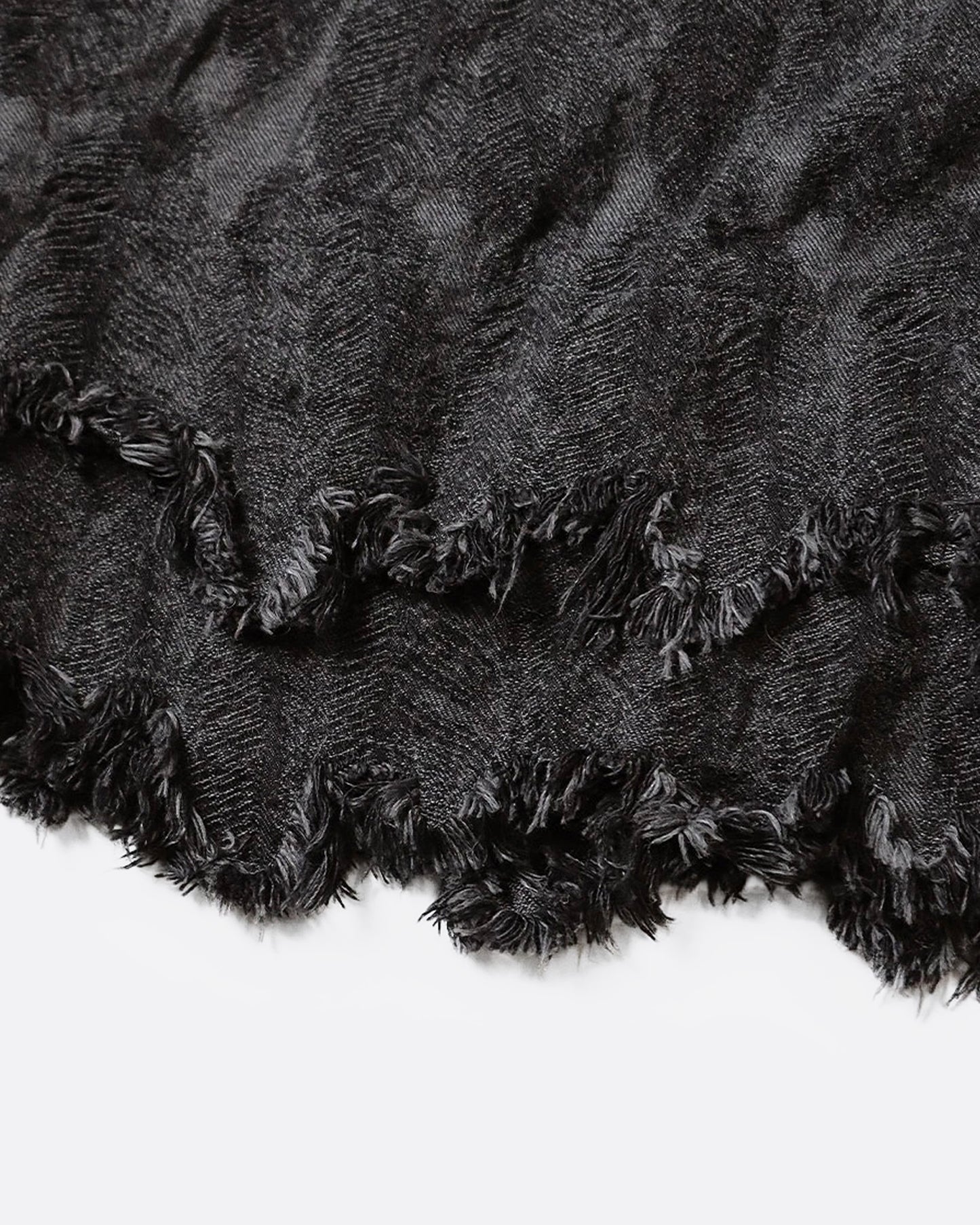 A close up of a jacquard denim bag with an all-over 3D feather motif and a cut-off hemline with a raw feathered seam.