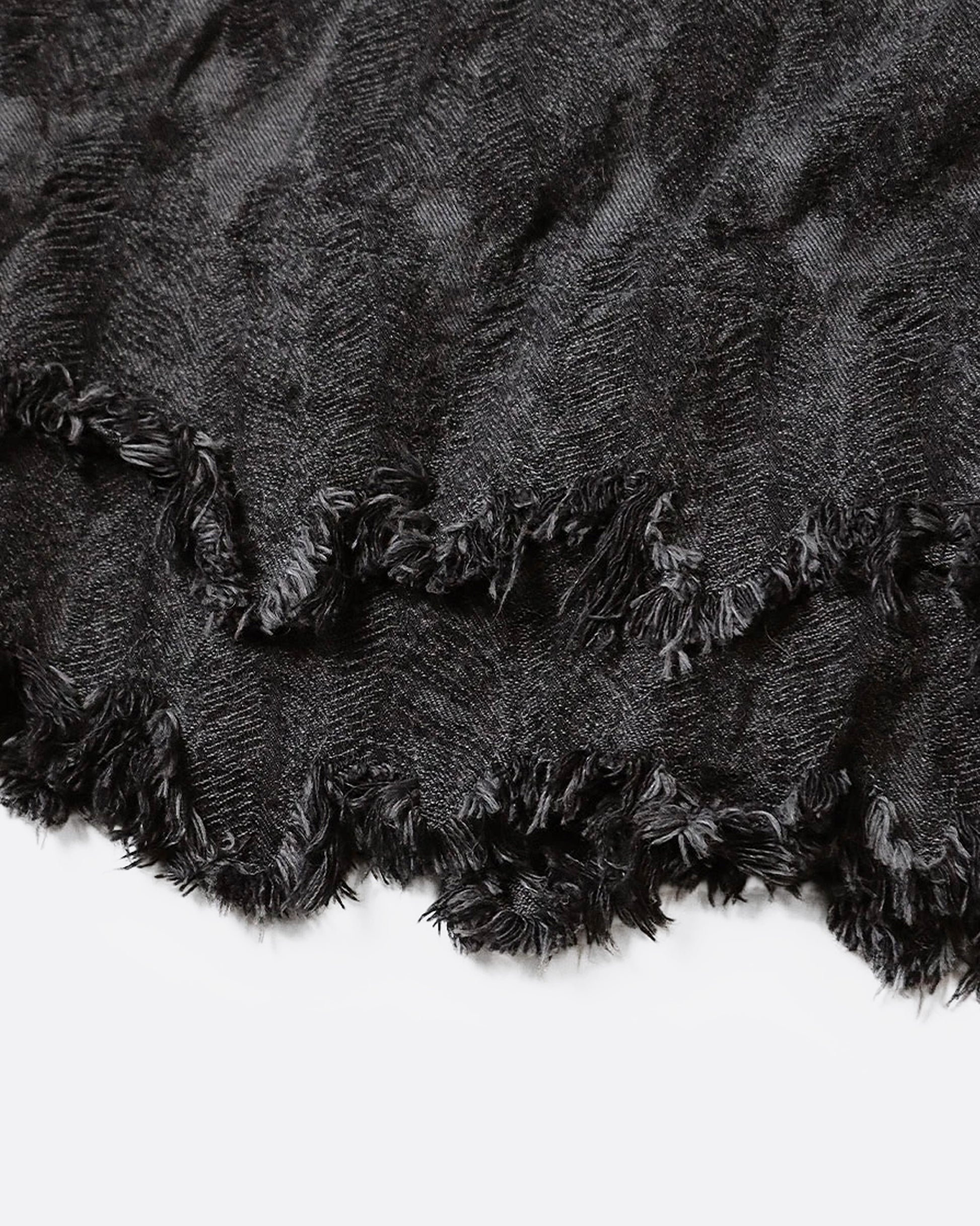 A close up of a jacquard denim bag with an all-over 3D feather motif and a cut-off hemline with a raw feathered seam.