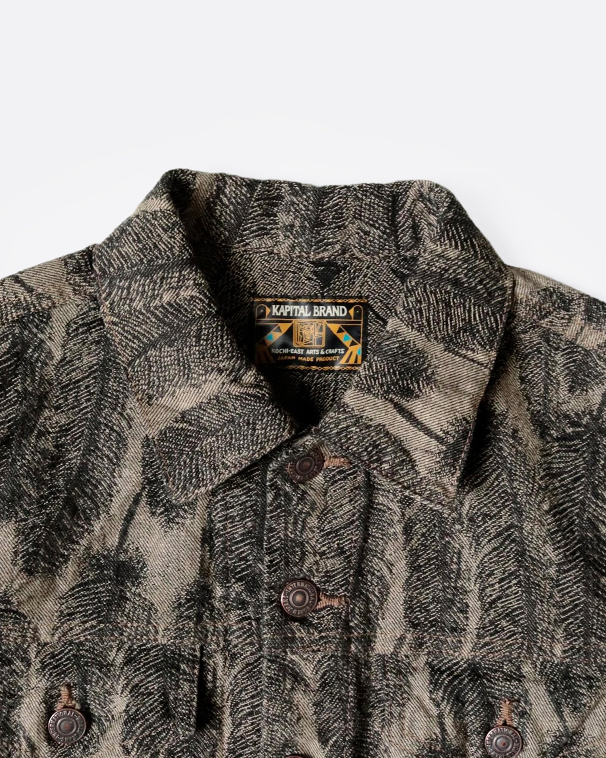A close up of a black and beige jacquard denim jacket with an all-over 3D feather motif and a cut-off hemline and raw feathered seam. Shown from the front.