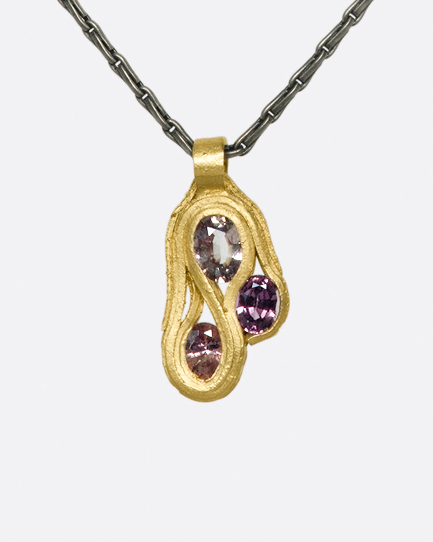 An organically shaped pendant featuring three oval pink sapphires enwrapped with 14k gold