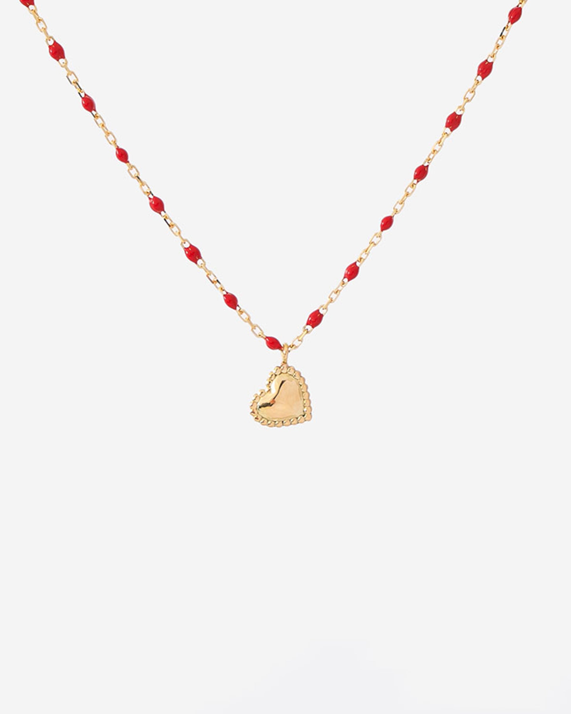 A thin yellow gold chain necklace with mini poppy red resin beads and a little dangling heart pendant.