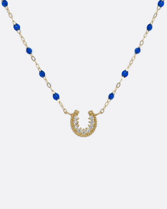 A yellow gold chain adorned with lapis blue resin beads and a lucky horseshoe pendant, lined with diamonds.