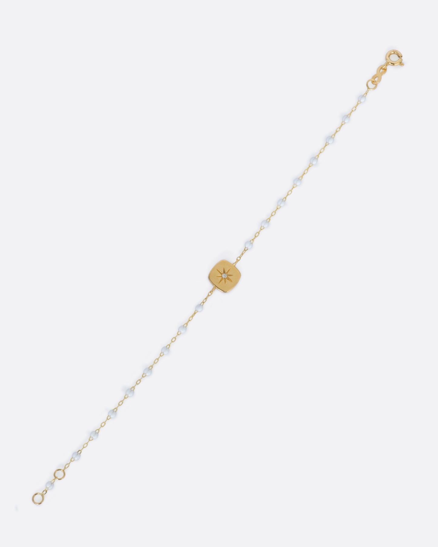 A classic yellow gold Gigi Clozeau necklace with white resin beads and a square tag pendant, with a star-set diamond at its center.