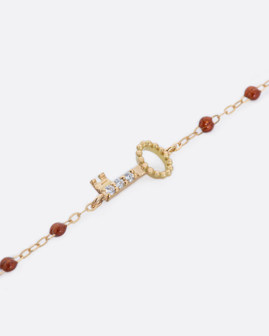 A yellow gold chain bracelet with copper resin drops and a key, lined in diamonds.