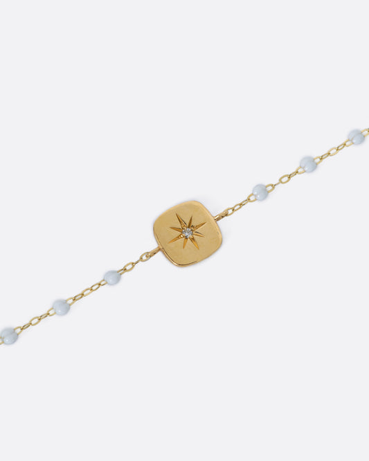 A classic yellow gold Gigi Clozeau necklace with white resin beads and a square tag pendant, with a star-set diamond at its center.