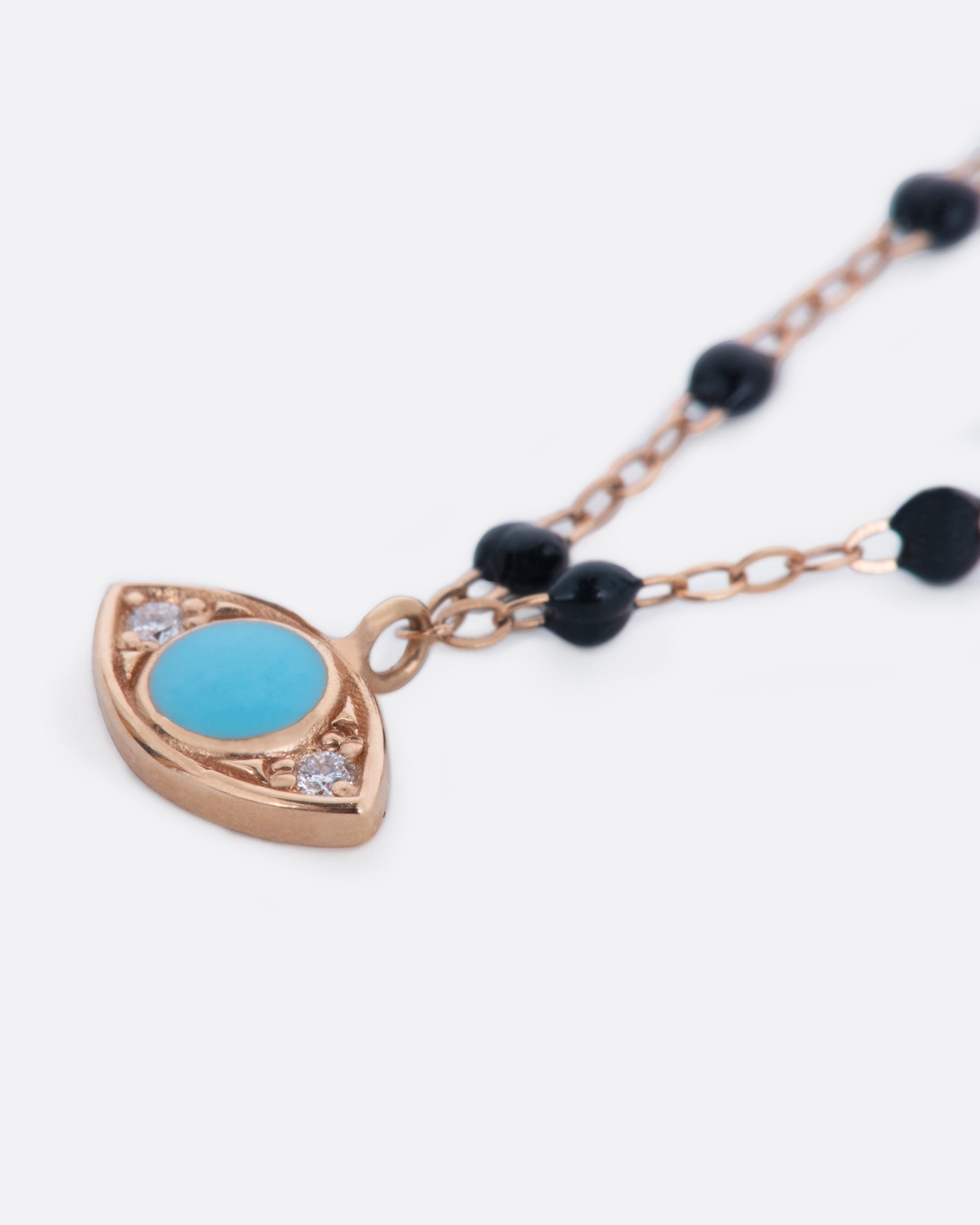 A rose gold chain necklace with black resin beads and an evil eye pendant.