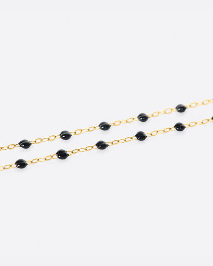 A close up view of a yellow gold cable chain necklace with black resin droplets. Shown from the side.