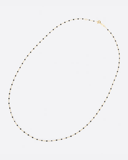 A yellow gold cable chain necklace with droplets of black resin. Shown clasped lying flat diagonally from the front.