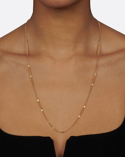 A long yellow gold multi chain necklace with alternating pattern of squares finished with gold solder. Shown from the front on a person.