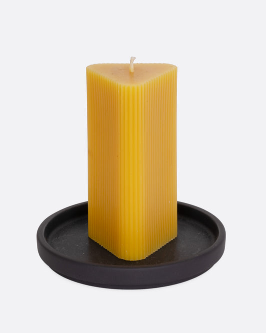 A triangular yellow candle on a black circular base, shown from the front.