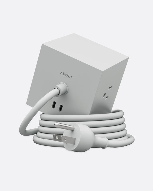 A gray cube shaped power strip with multiple outlets and a coiled cable, shown from the back.