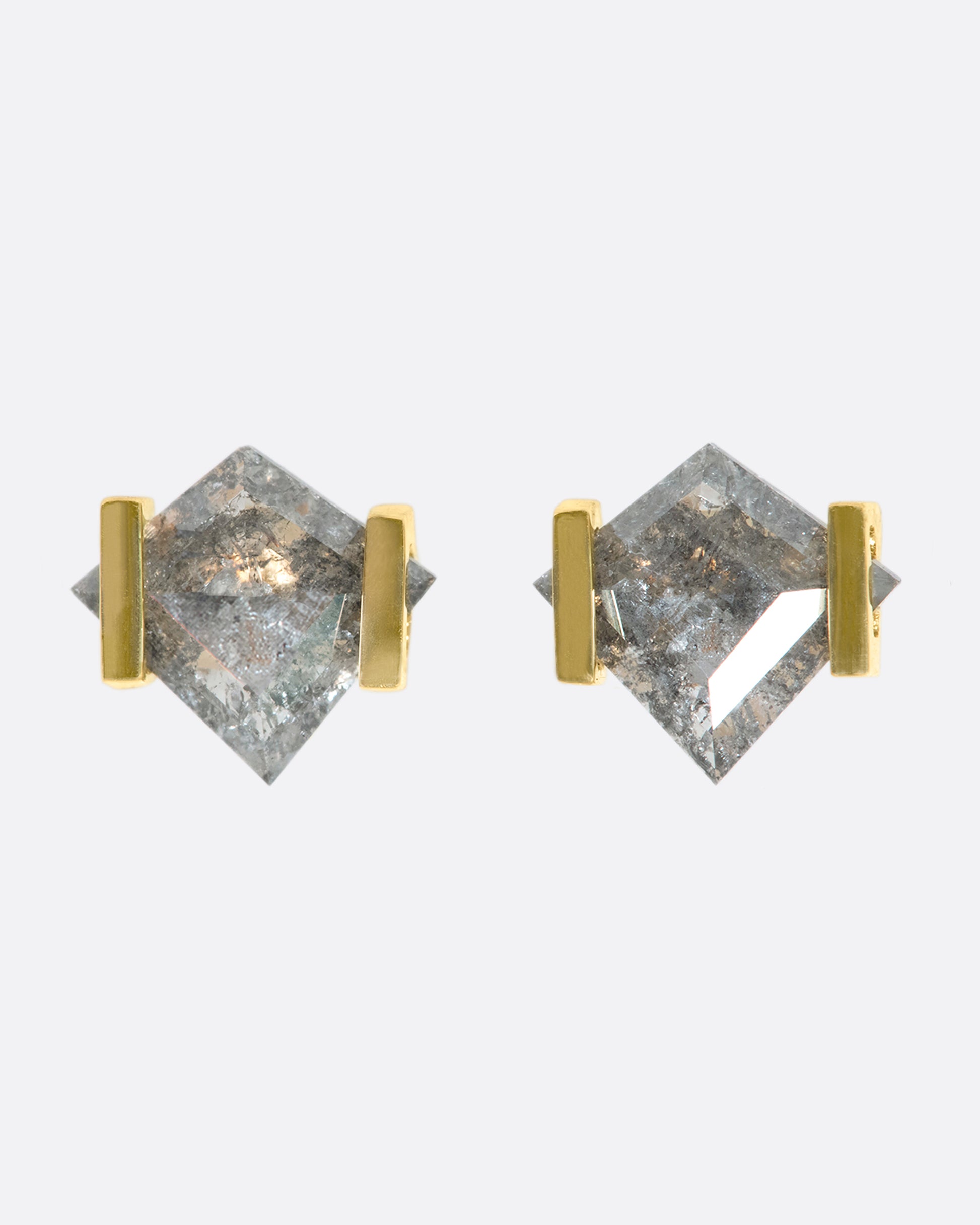 A close up of a pair of kite shaped grey diamonds in delicate gold settings.