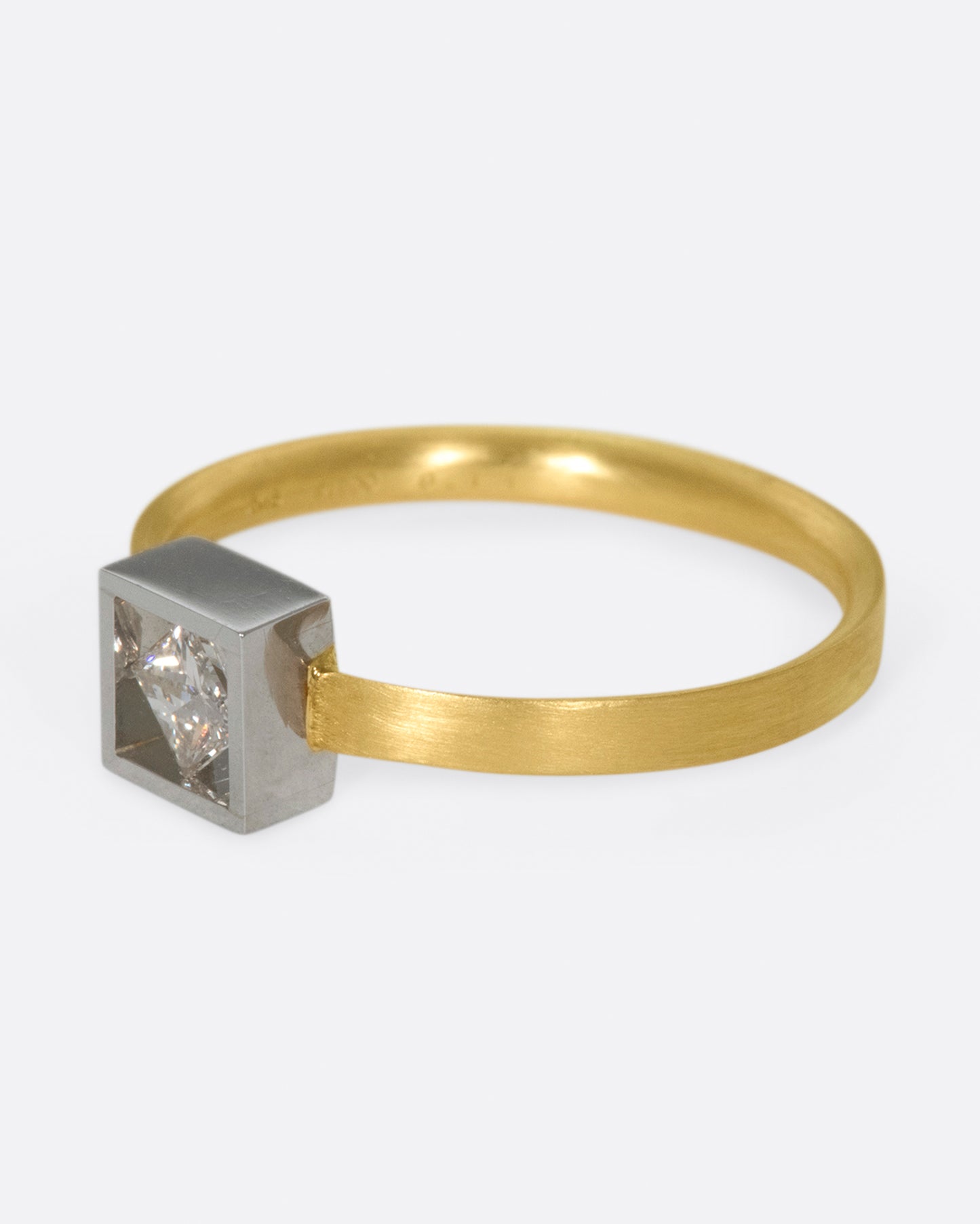 A geometric solitaire ring with a princess cut diamond set on its side in a platinum setting on a yellow gold band.