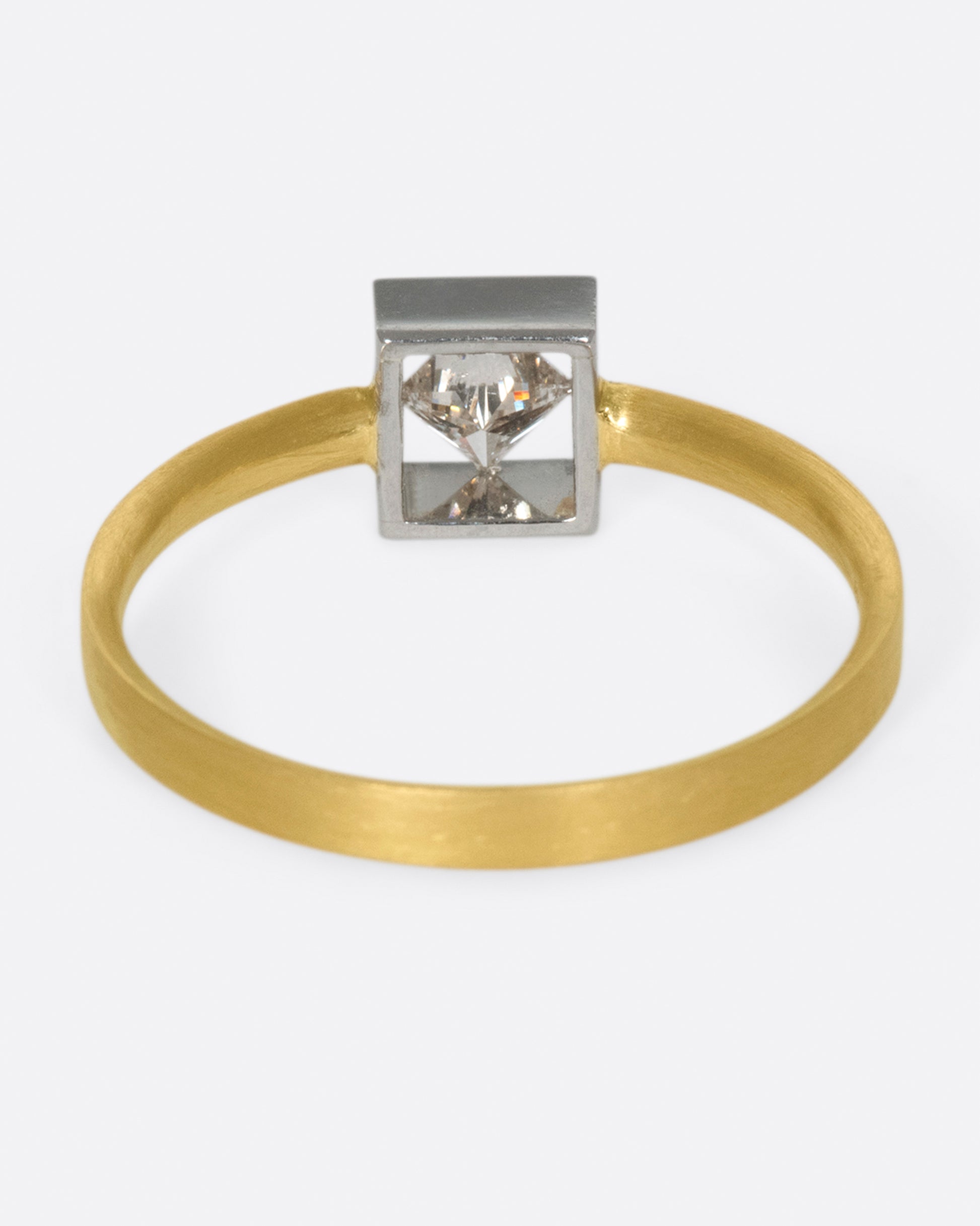 A geometric solitaire ring with a princess cut diamond set on its side in a platinum setting on a yellow gold band.