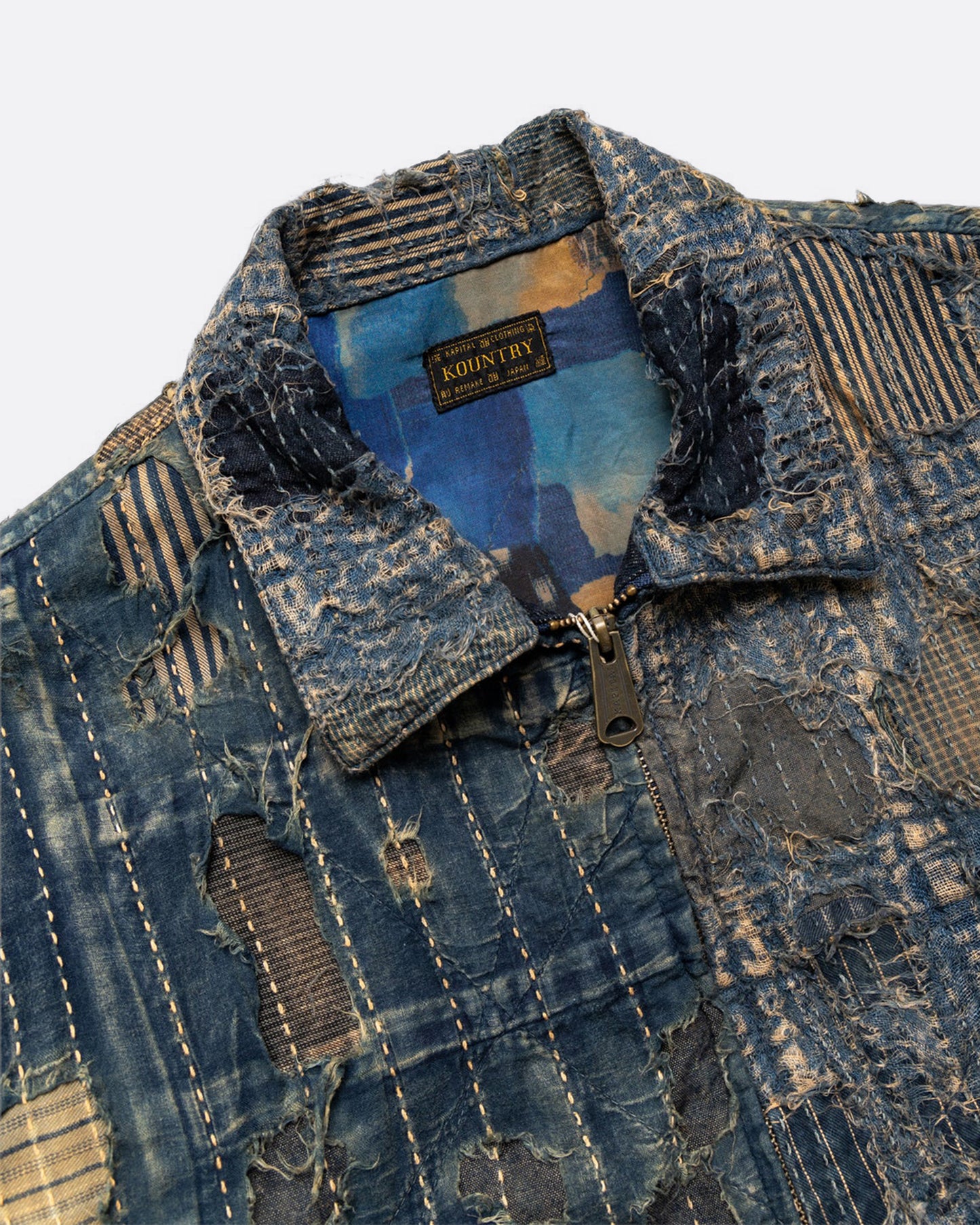 Distressed and repaired patchwork indigo jacket with pockets and front zipper. View close up of the collar and zipper pull.