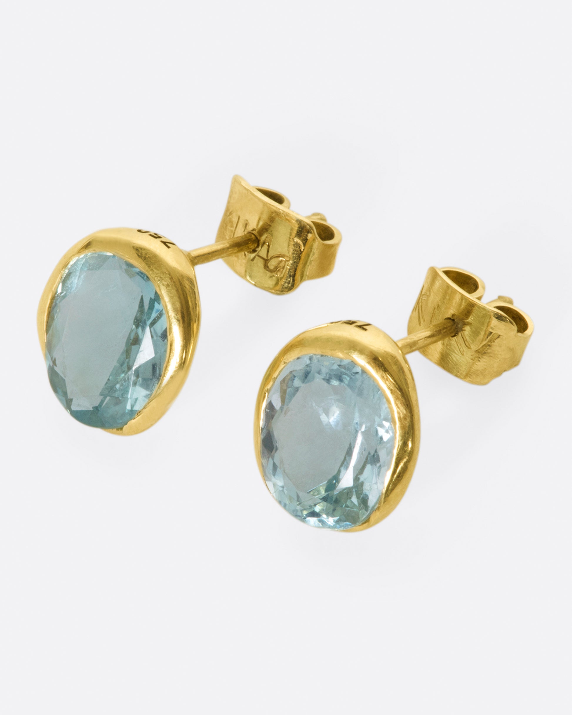 A pair of yellow gold and aquamarine solitaire stud earrings, shown from the side.