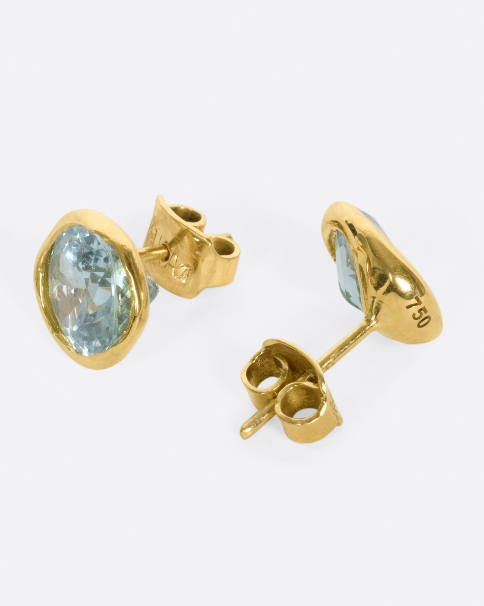 A pair of yellow gold and aquamarine solitaire stud earrings, shown from the side.
