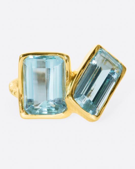 A yellow gold ring featuring two large emerald cut aquamarines set slightly askew