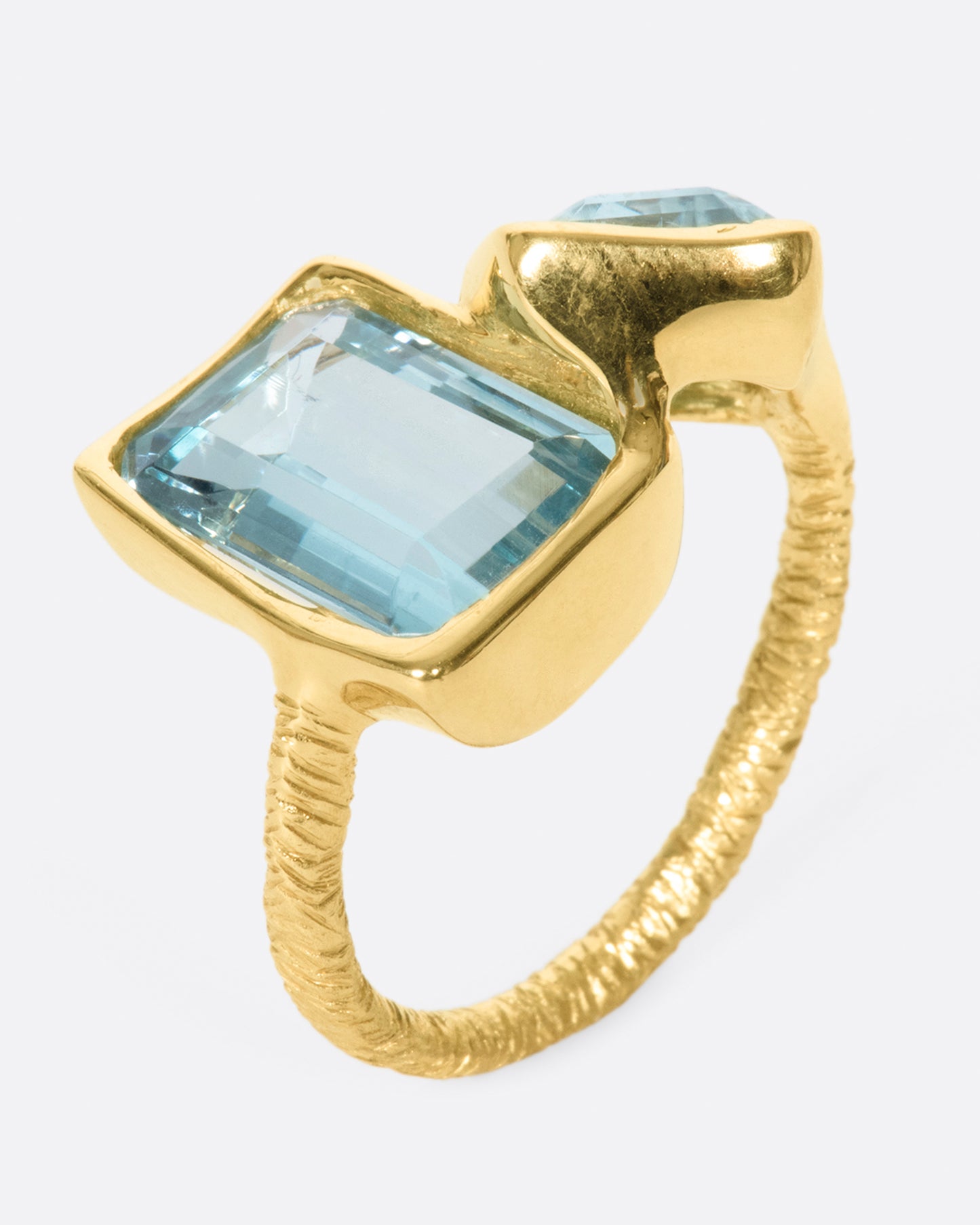 A yellow gold ring featuring two large emerald cut aquamarines set slightly askew