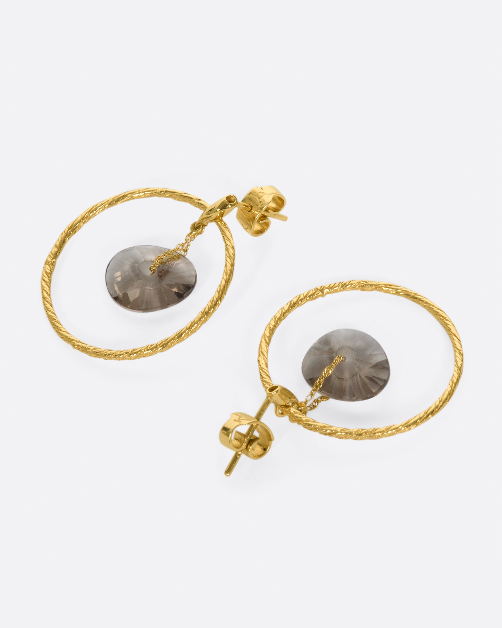 A pair of circular yellow gold wire earrings with smokey quartz donut-shaped beads hanging freely in the middle, shown laying flat.