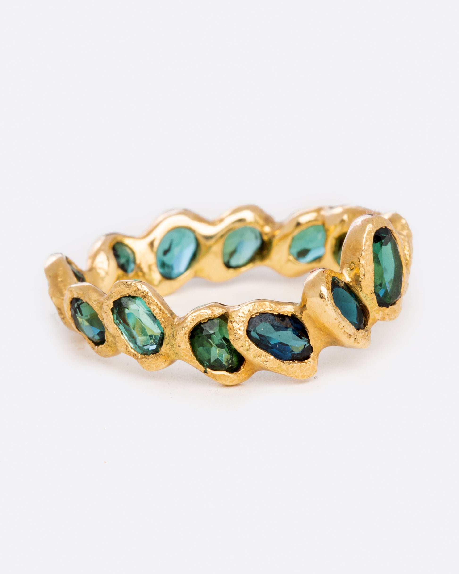 A yellow gold eternity band ring with oval blue green tourmalines, each set facing slightly askew.