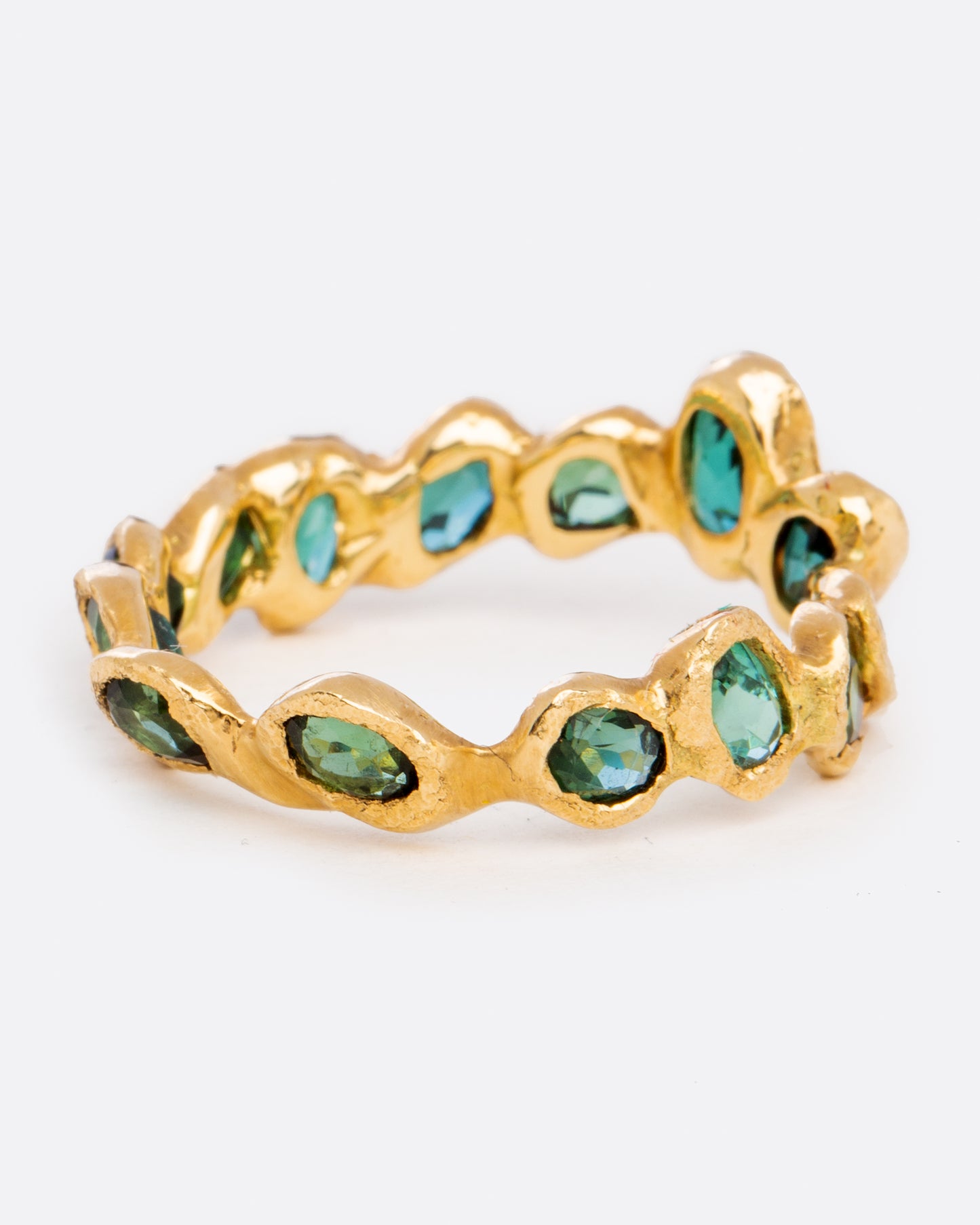 A yellow gold eternity band ring with oval blue green tourmalines, each set facing slightly askew.