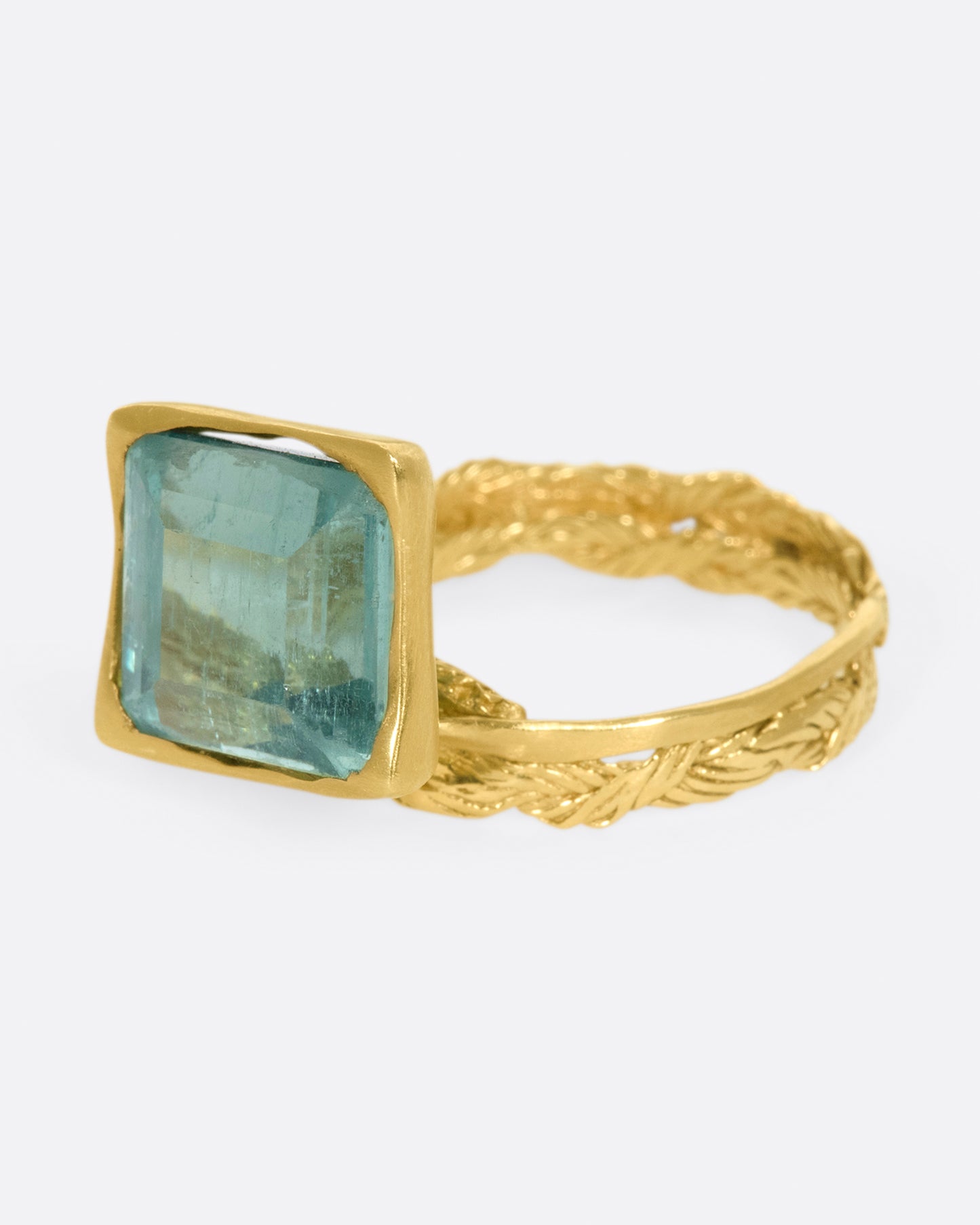 A gold braided band with a pale green square tourmaline.