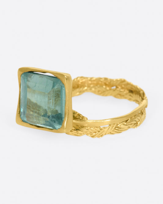 A gold braided band with a pale green square tourmaline.