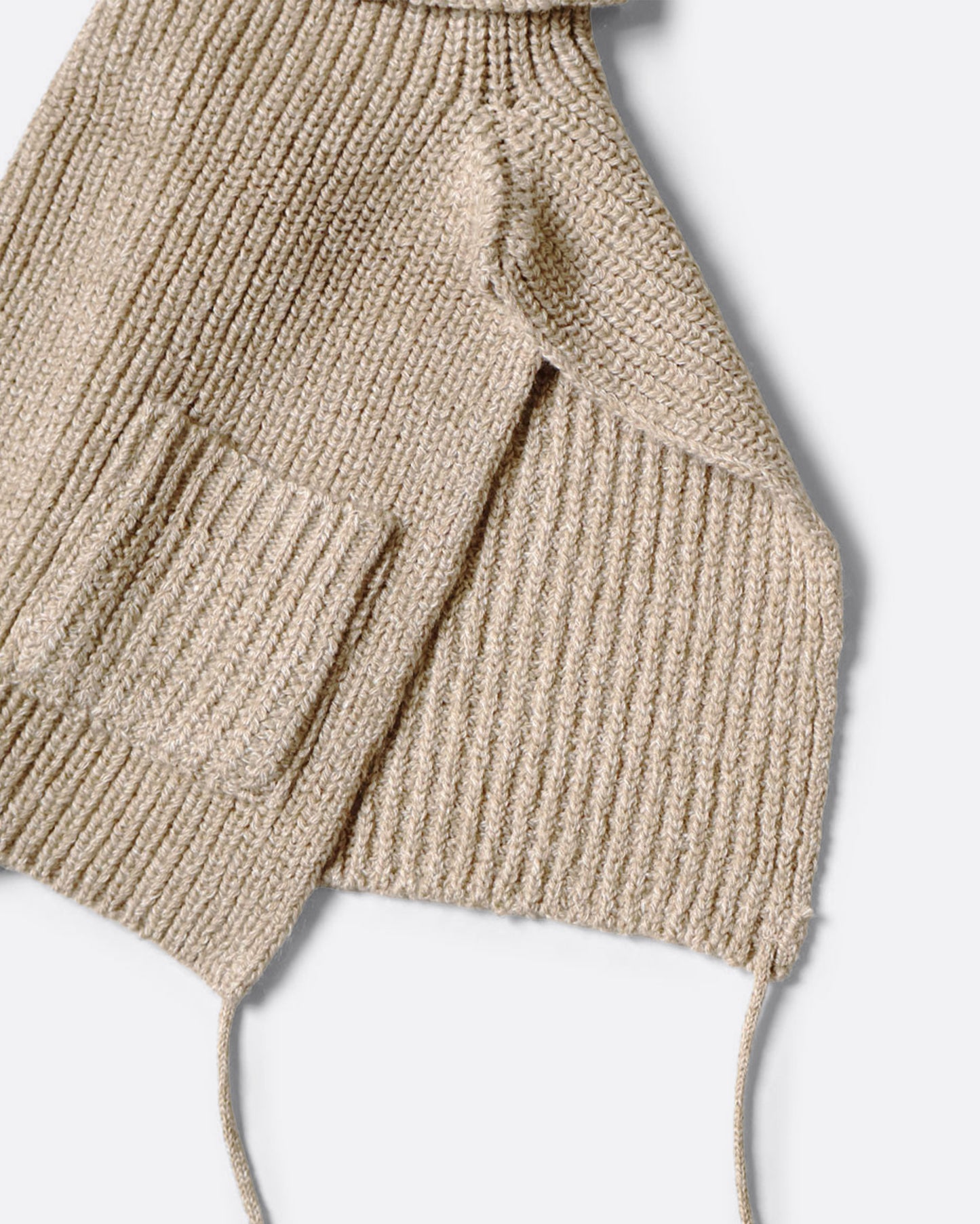 A close up of a beige loose knit bib poncho with a front pocket, long tassels, and a high neck.