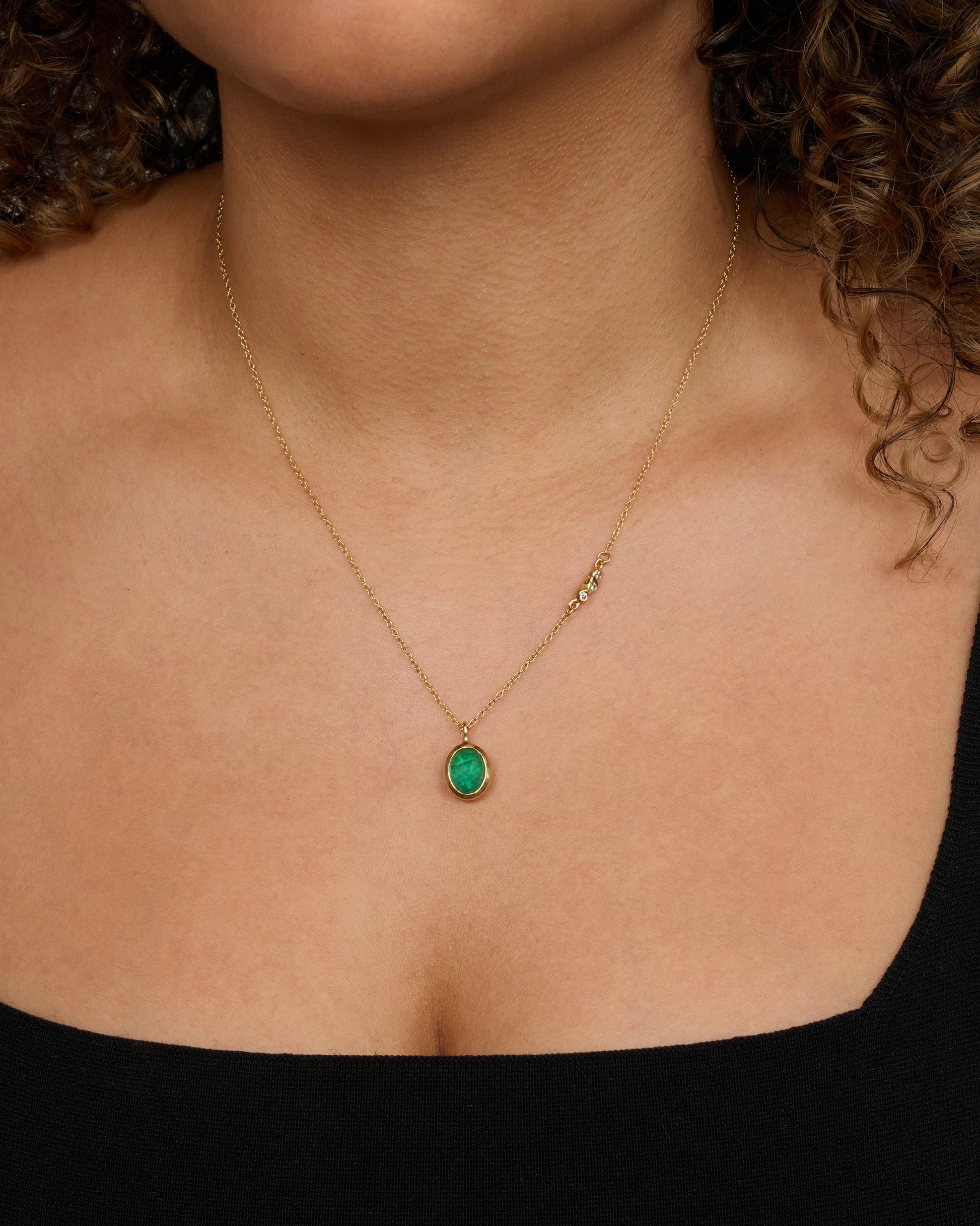 A yellow gold necklace with an oval cabochon emerald pendant and triple diamond cluster spacer. View of the necklace worn.